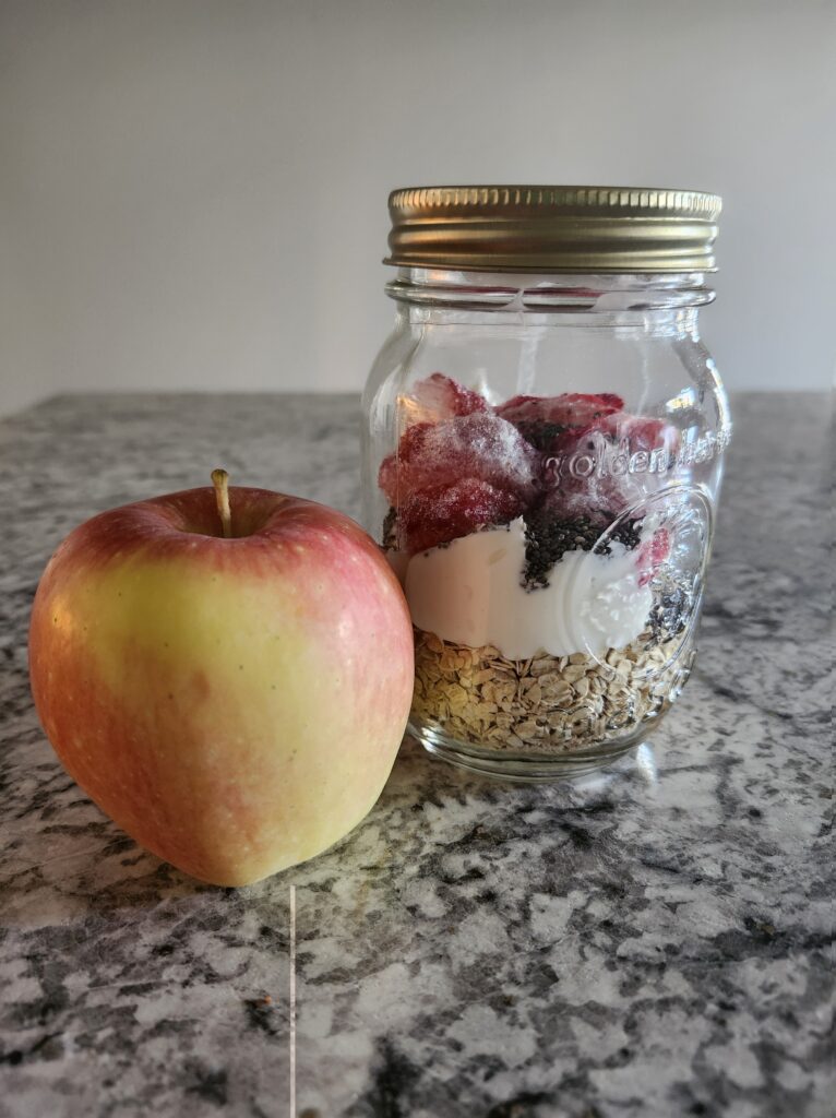 Overnight oats in a mason jar and apple on the couter ready to be eaten.