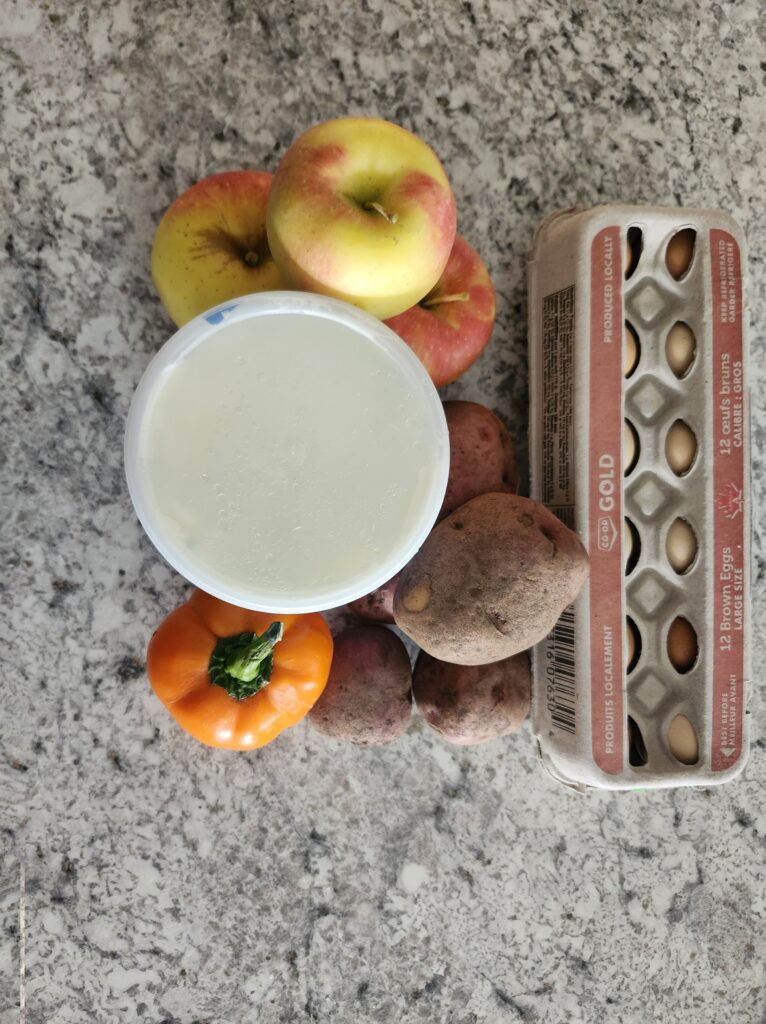 Carton of eggs, greek yogurt, potaotes, apples and peppers on the counter