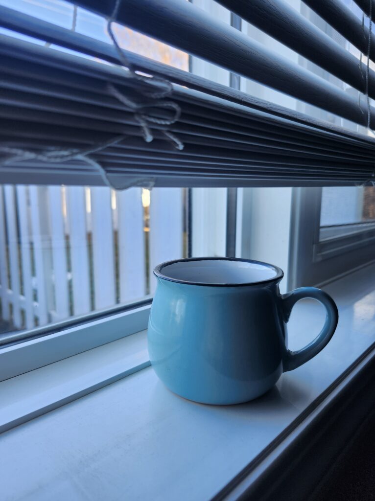 Morning cup of coffee on window sil wih blinds half open