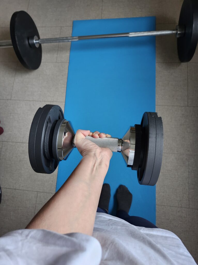 Weight training holding a dumbbell and weight plates and barbell on a blue mat