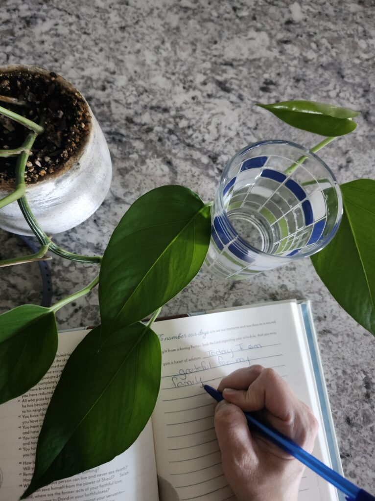 Journaling with hand on the counter by a plant and a glass of water.
