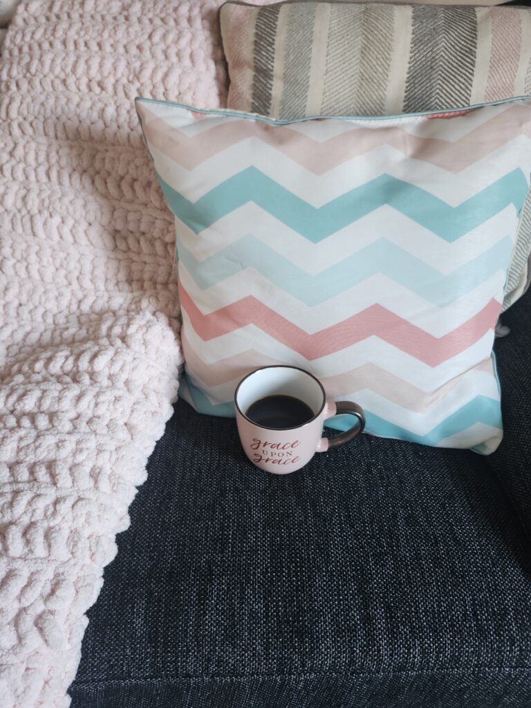 Cup of coffee on a couch with cozy pillows and a blanket for relaxing