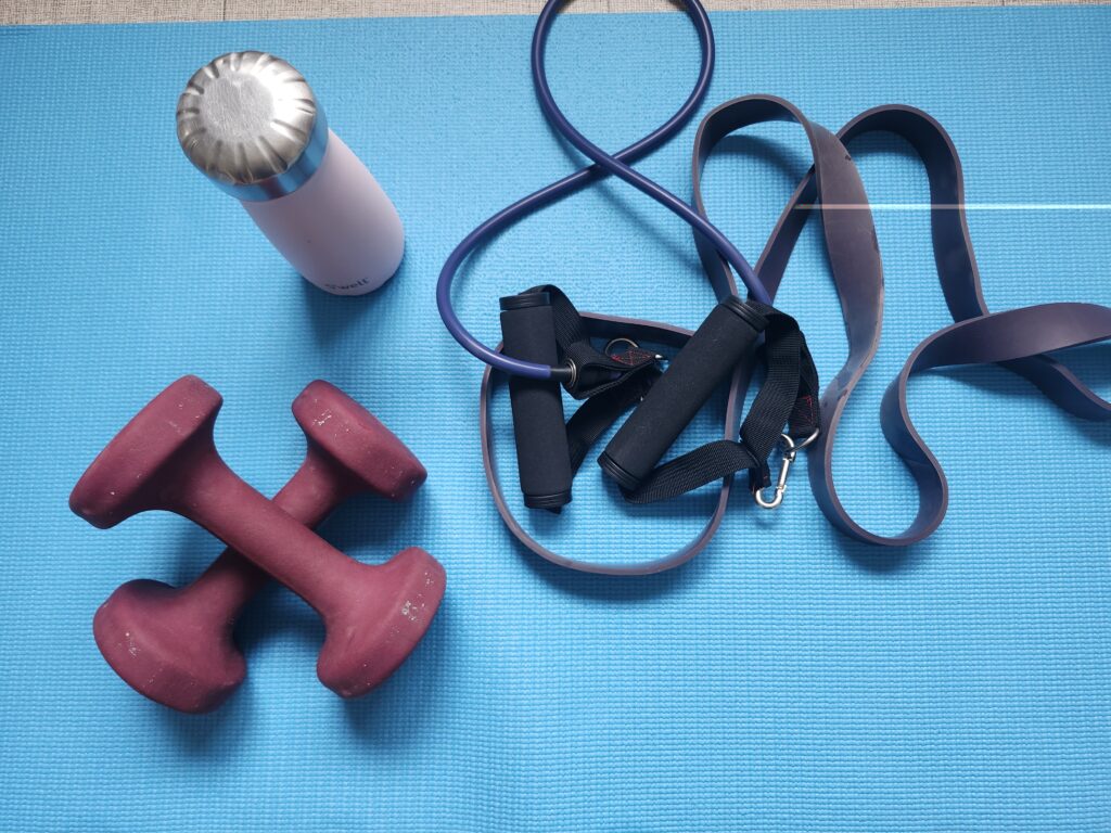 Red dumbbells resistance bands and a water bottle on a blue mat
