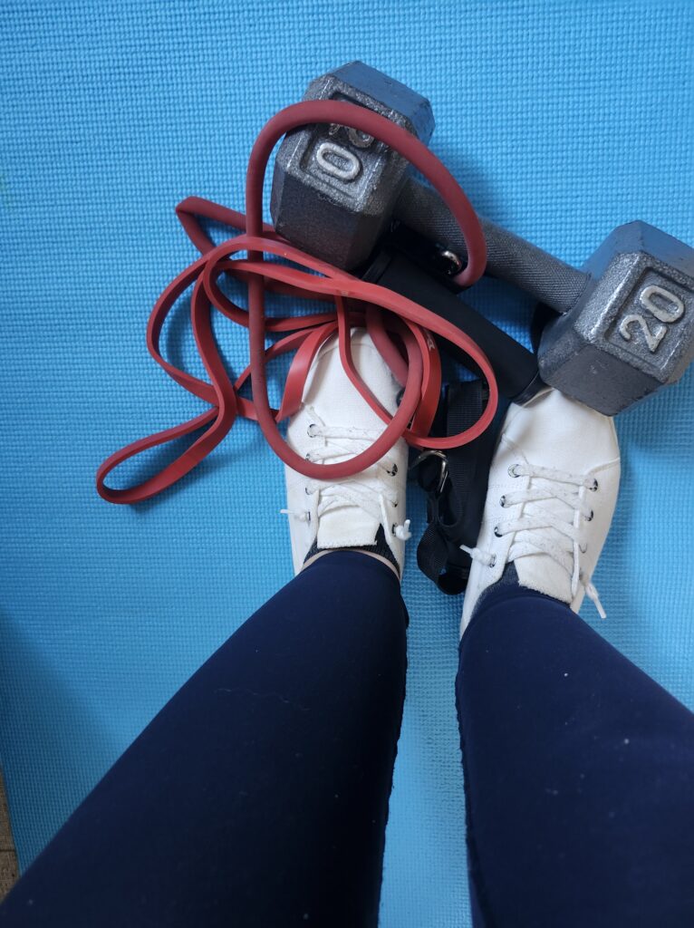 Reistance bands and a dumbbell on a blue mat with feet showing from a downward angle