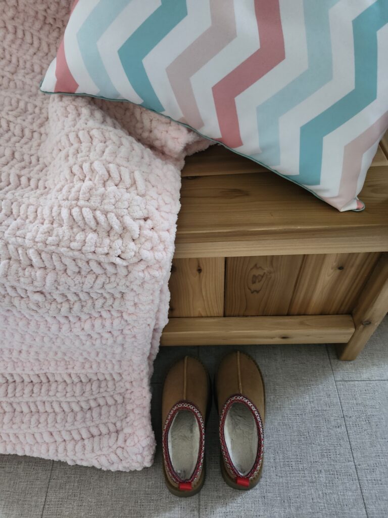 Slippers under a cozy bench with pillow and a blanket