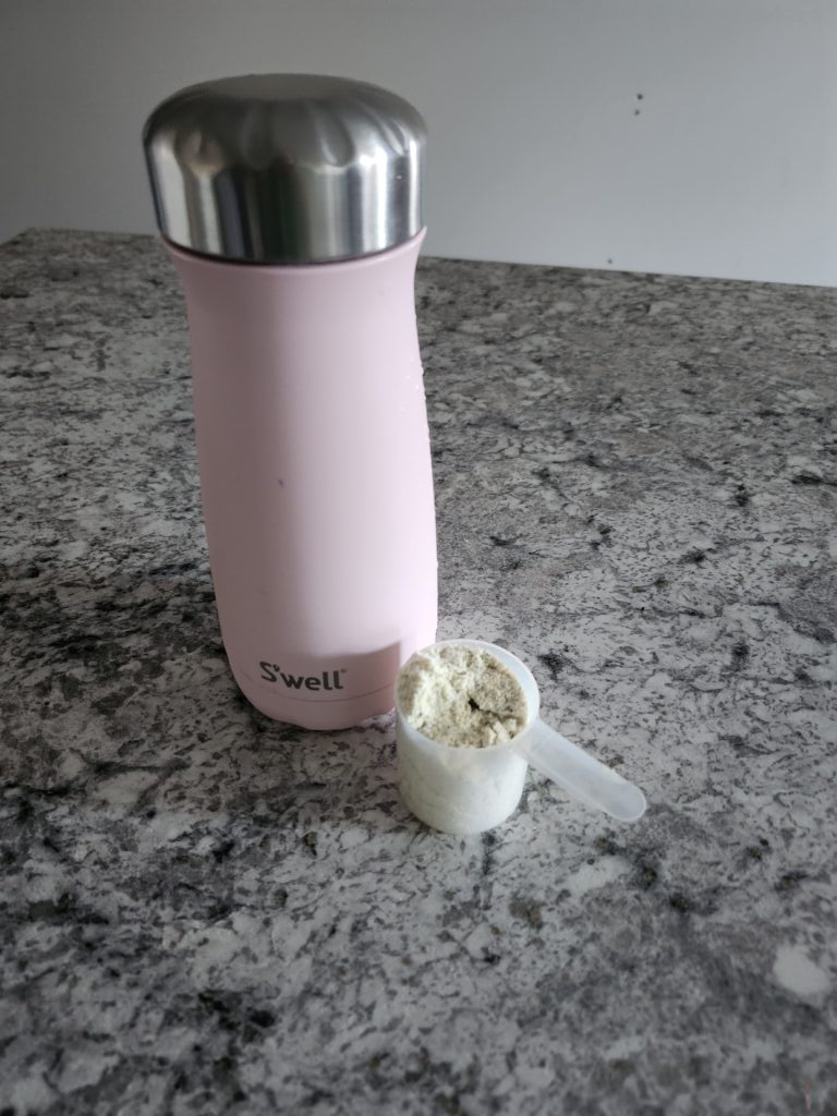 Pink water bottle with scoop of protein powder beside it ready to mix it up