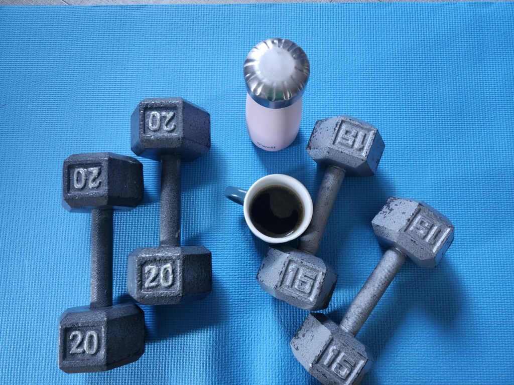 Two pairs of dumbbells with a water bottle and cup of coffee on a blue mat after a workout