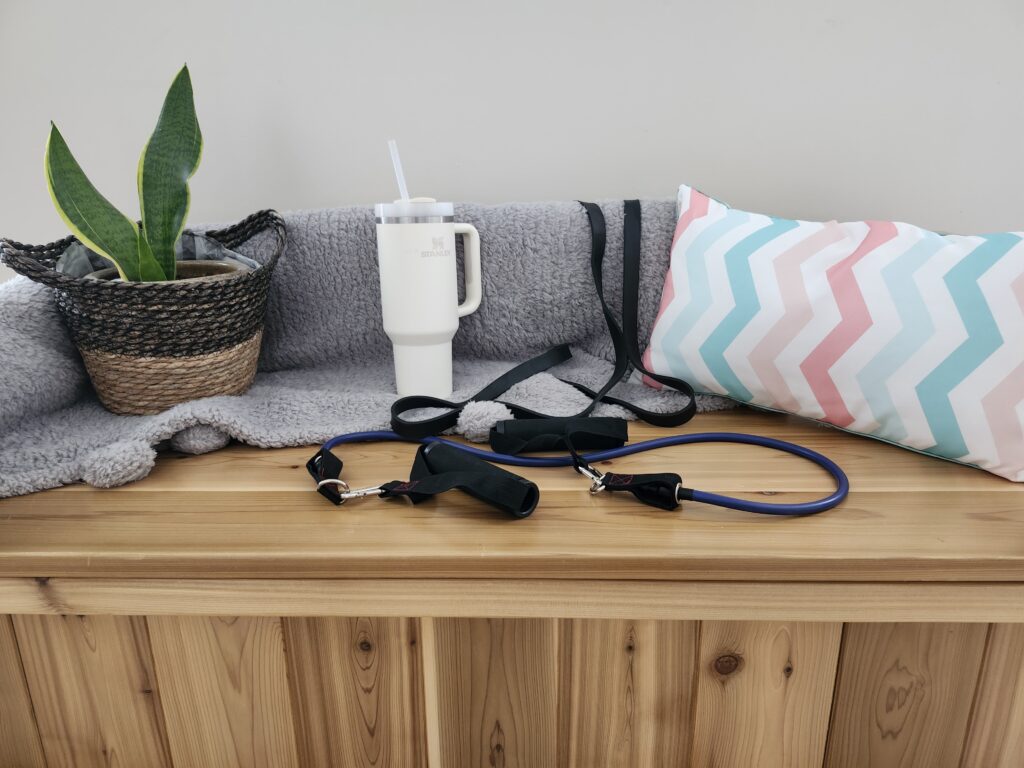 Cozy gym corner with resistance bands, water bottle a plant and a pillow on a bench to create a cozy space for working out