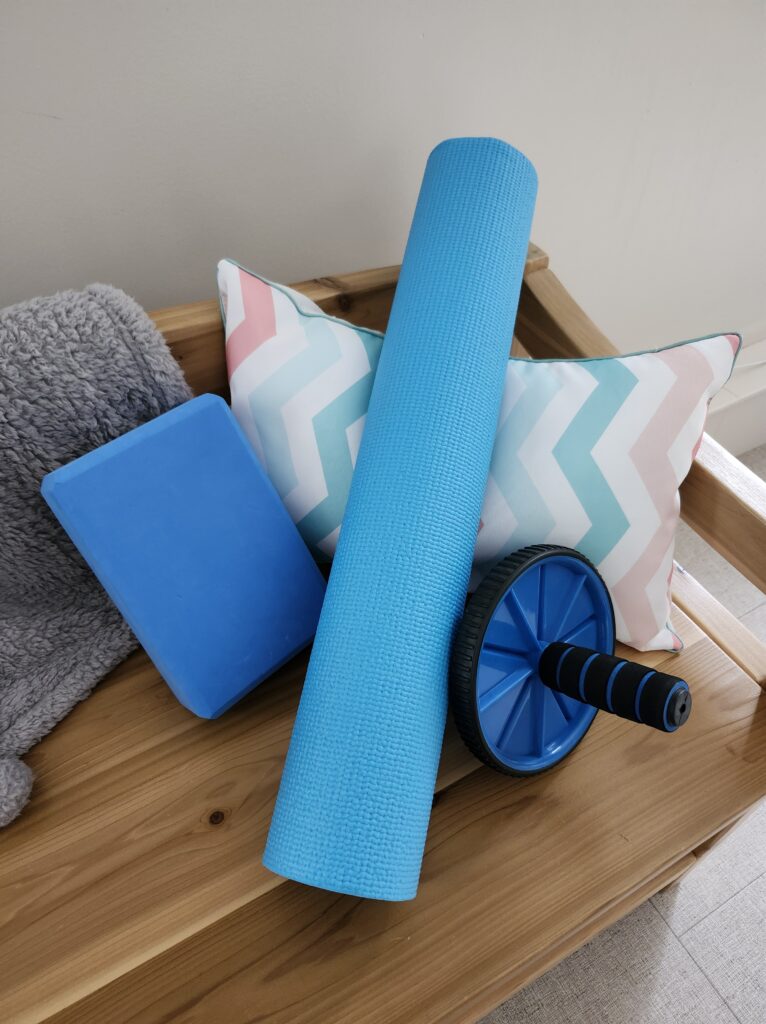 Rolled up yoga mat, ab roller, yoga block on a bench preparing for active rest day