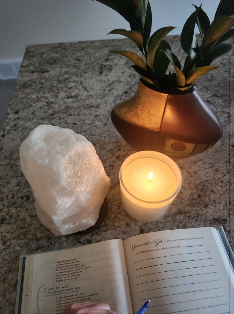 A soft candle and salt lamp and plant on the counter with a journal
