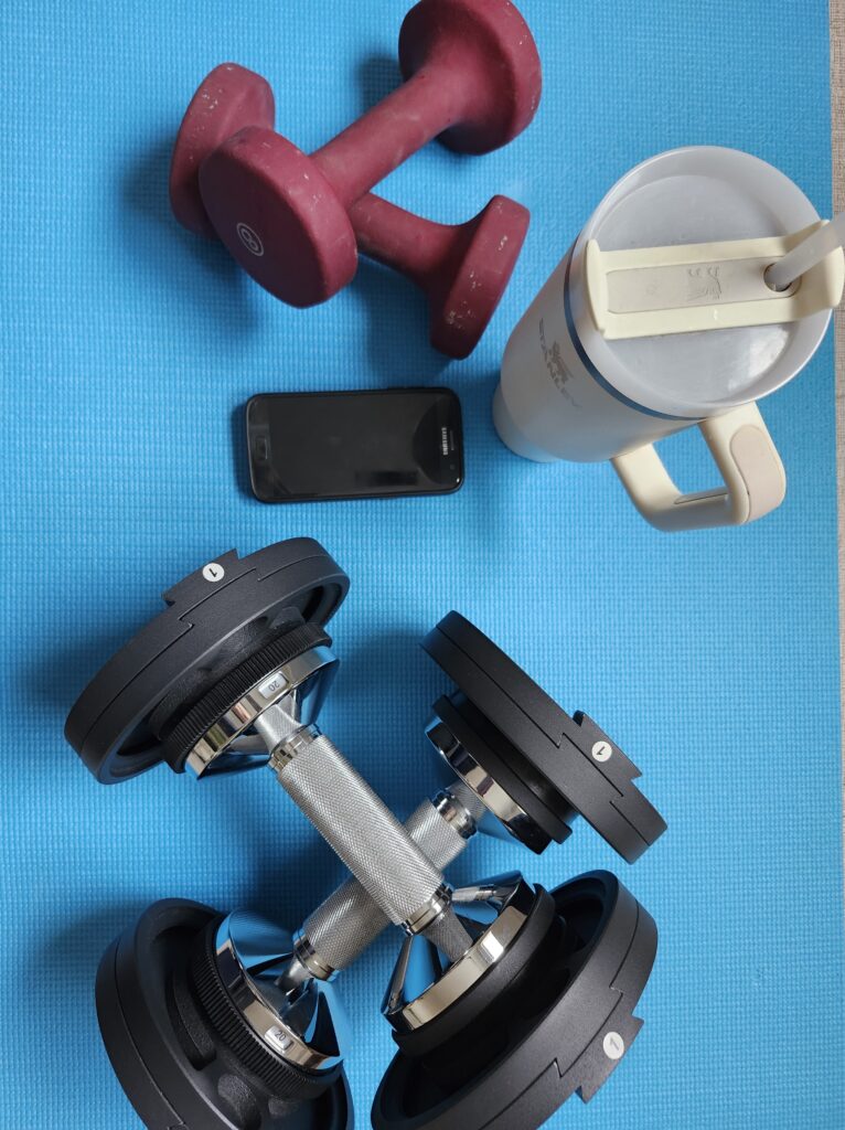 Preparing to workout on a blue mat with adjustable weights, water bottle and a timer