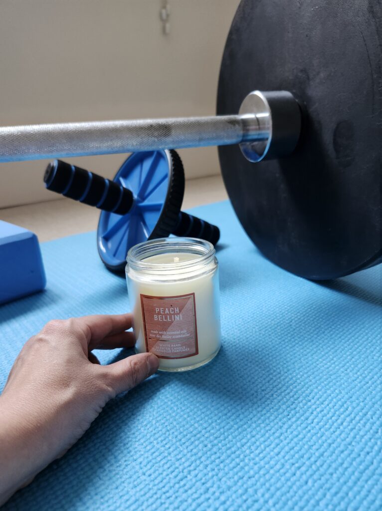 Ab roller, weight plate, yoga block on a blue mat with a candle. Create a relaxing spot
