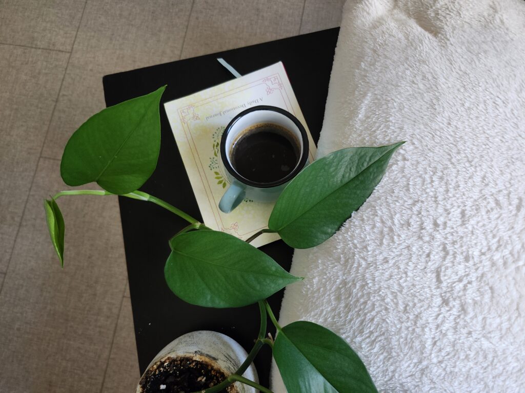Cozy bedroom with a folded blanket on a side table with a journal, plant and coffee for relaxing