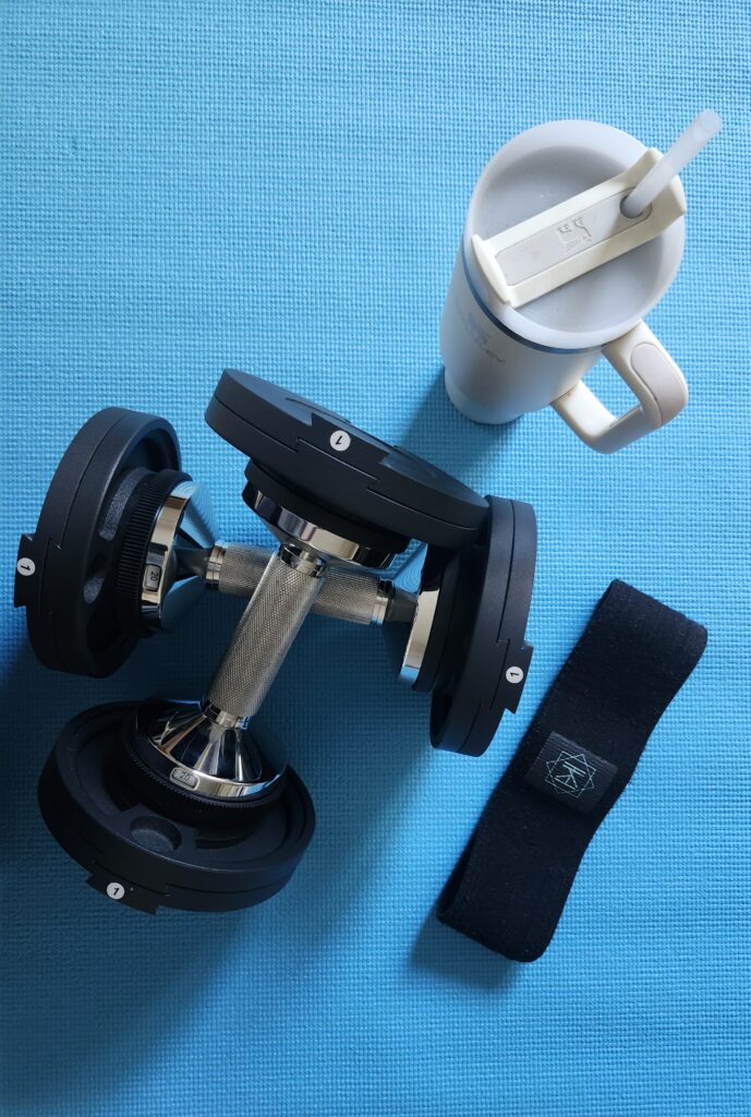 Close up of dumbbells, bands and water bottle on a yoga mat to help with daily steps towards strength and energy in midlife