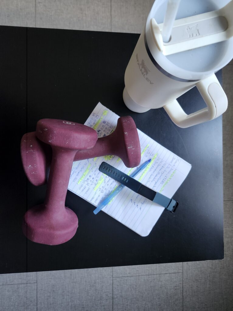weights, journal pen, tracker and water bottle on a table