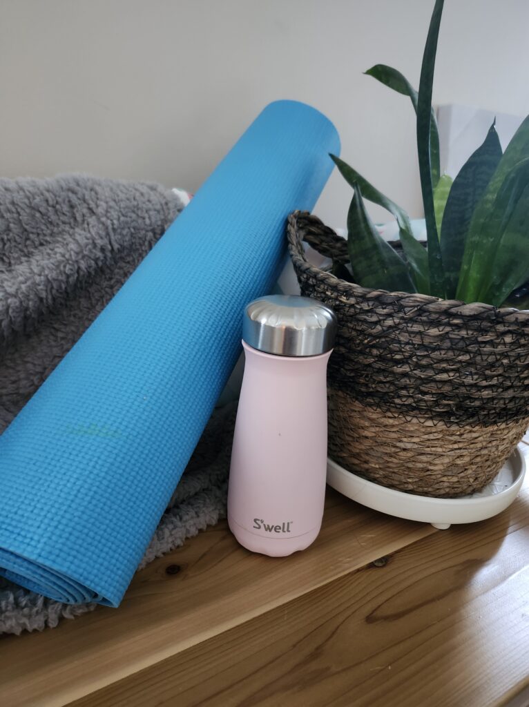 Rolled up yoga mat on a bench with a plant and water bottle to create a peaceful workout space